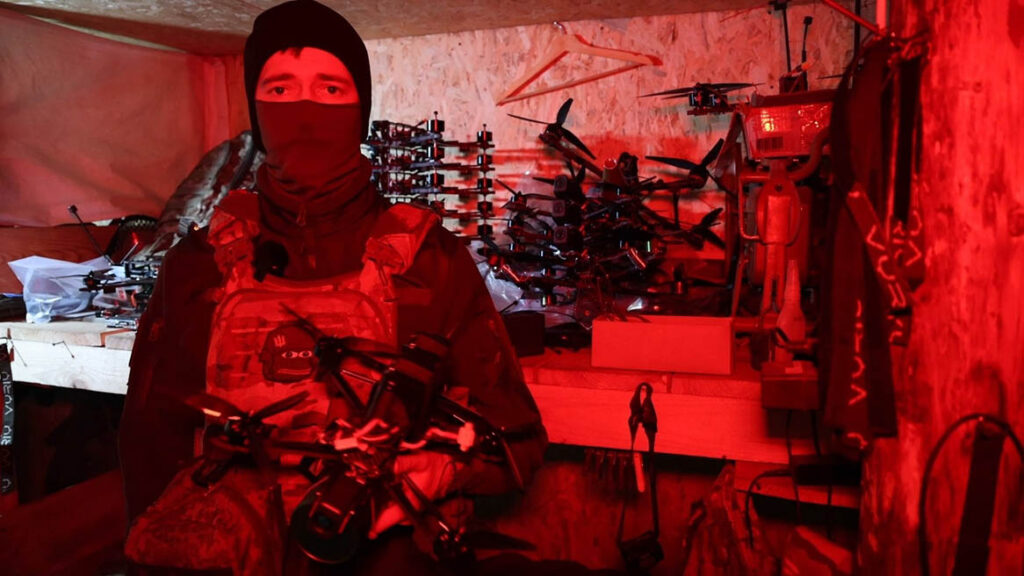 A Ukrainian FPV operator stands inside a shelter, with stacks of RF-controlled FPV drones behind him. Mass ultimately still matters greatly, and as such, ‘regular’ RF-controlled FPVs will continue to be a common sight in Ukraine’s skies for the foreseeable future. (State Border Service of Ukraine)