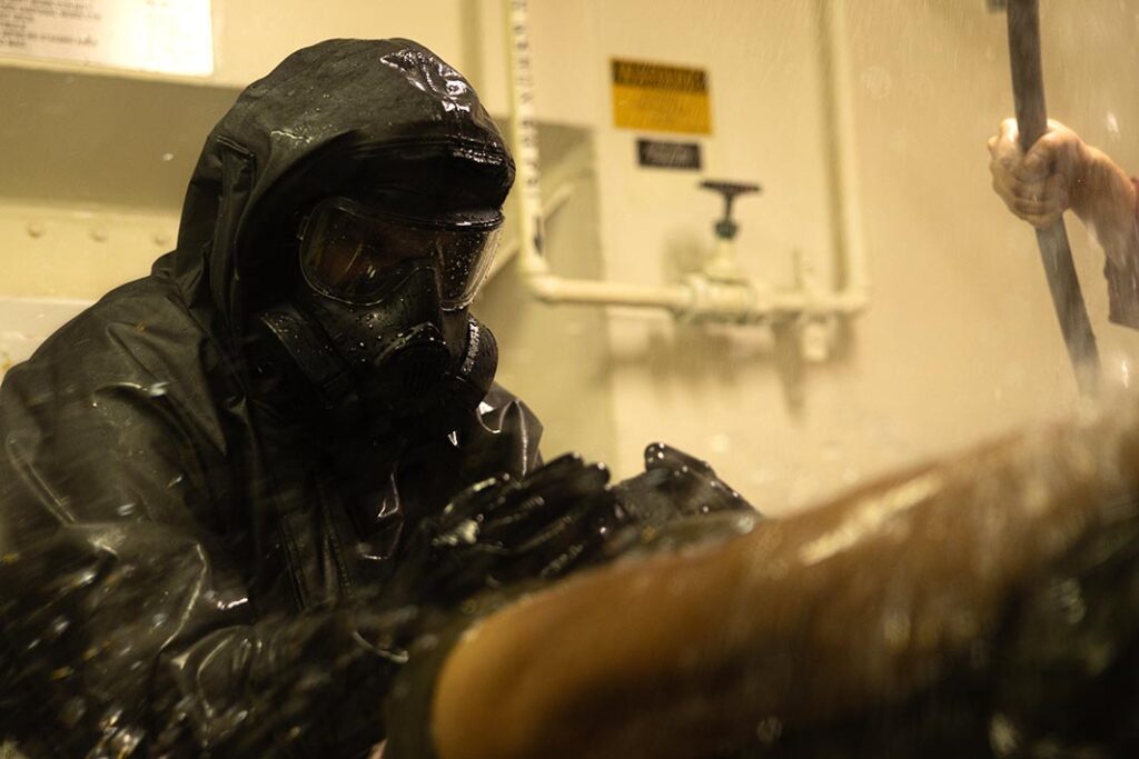 A USMC CBRN specialist with the 31st Marine Expeditionary Unit assists with decontaminating a simulated casualty during chemical decontamination training aboard the USS America (LHA 6), in the Coral Sea, on 25 June 2025. (USMC/LCpl Gerardo Mendez)