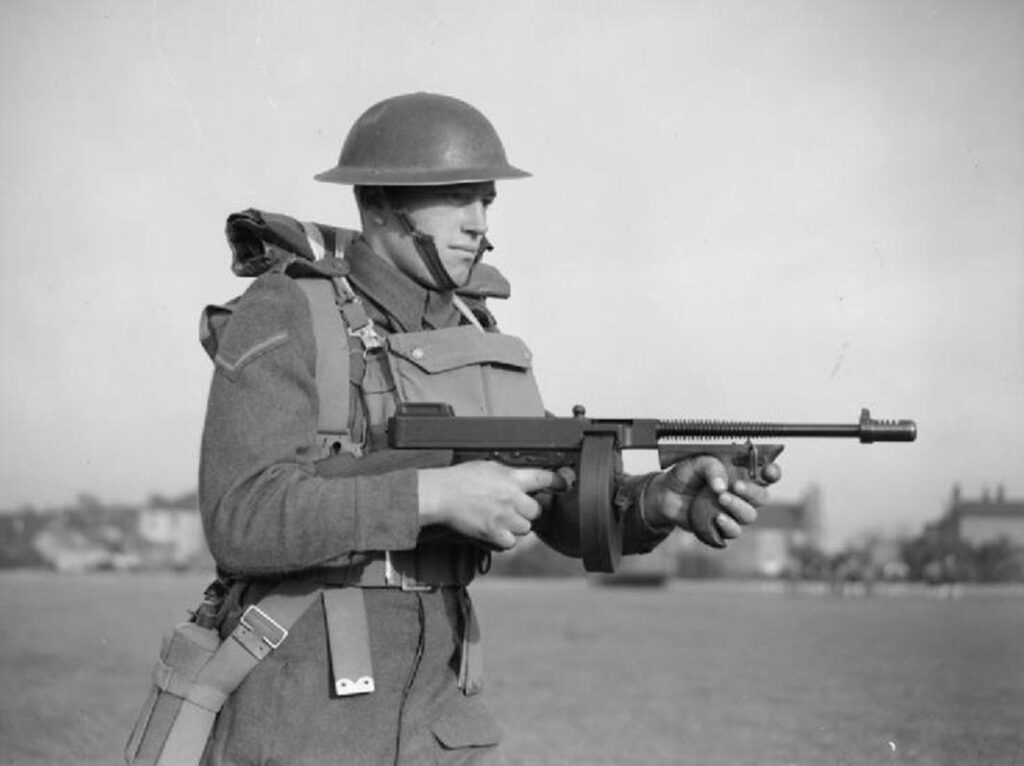 A lance-corporal of the East Surrey Regiment poses with a Thompson SMG, at Chatham, Kent, 25 November 1940. (War Office/Putnam; via Wikimedia Commons; Public Domain)